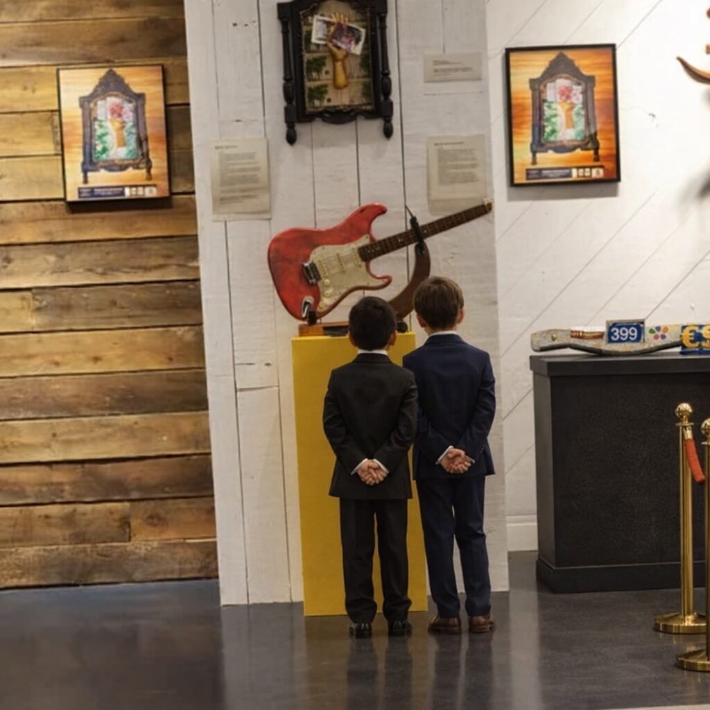 Exposición de arte objeto JSUS ART DELUXE con escultura de guitarra eléctrica rosa y visitantes. Galería de arte contemporáneo con obras exclusivas de lujo.